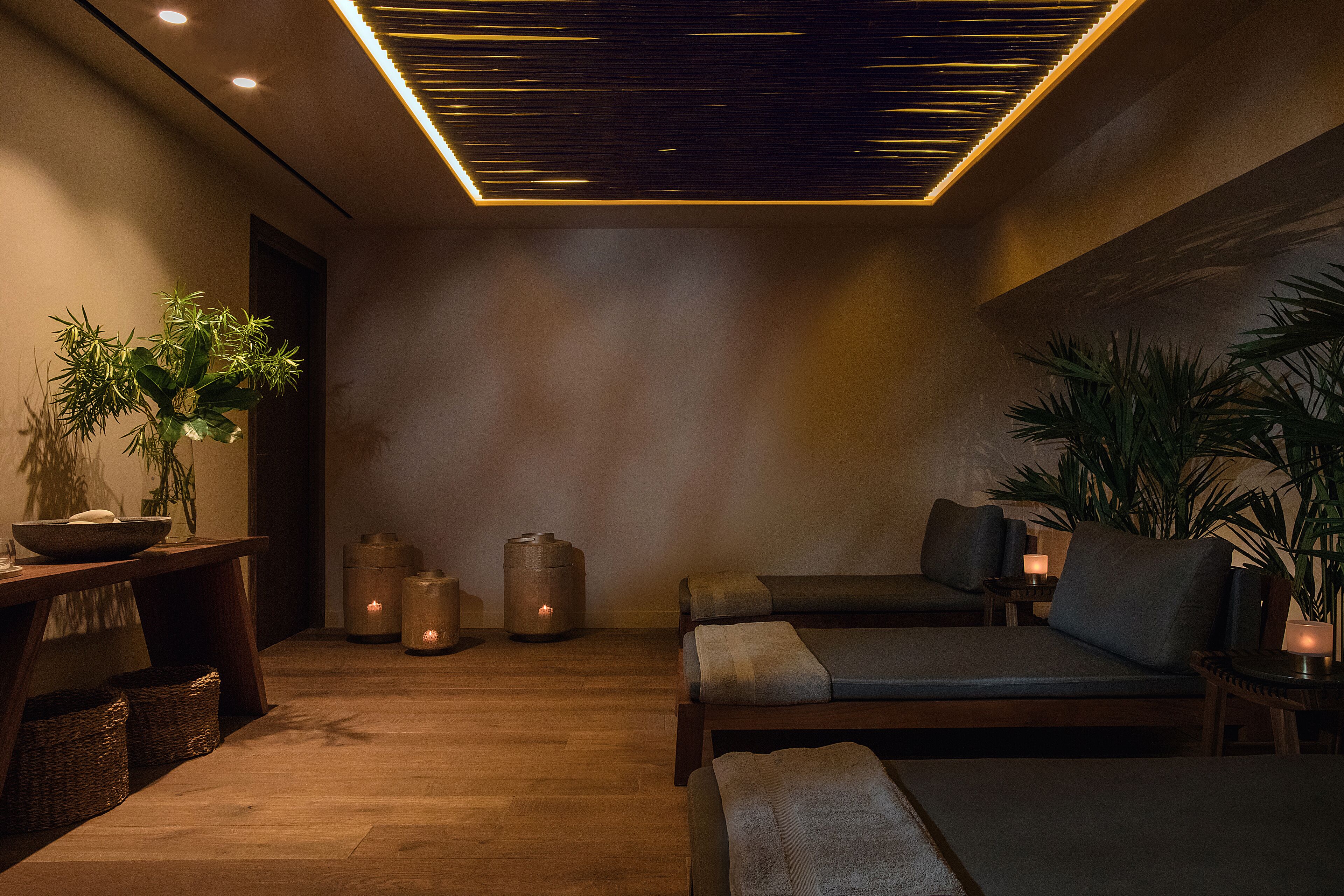 A spa room with wooden flooring, two reclining chairs, a table with a bowl and plant, and candles.