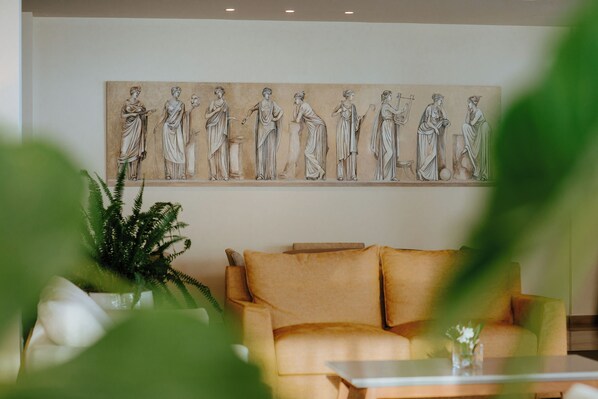 A room with a beige sofa, a coffee table, and a large wall mural depicting classical figures.