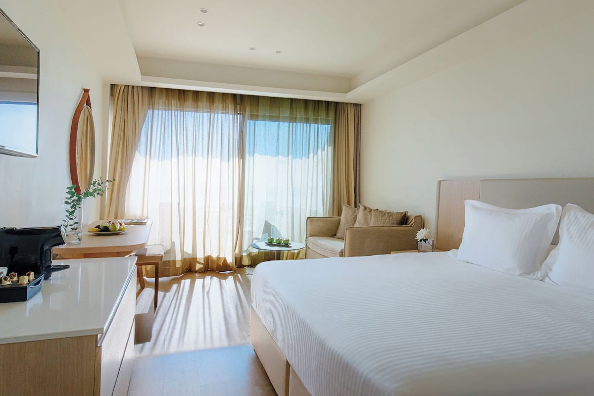 Une chambre d’hôtel avec un grand lit, un bureau avec une chaise, un canapé et une table à manger agrémentée d’un vase de fleurs.