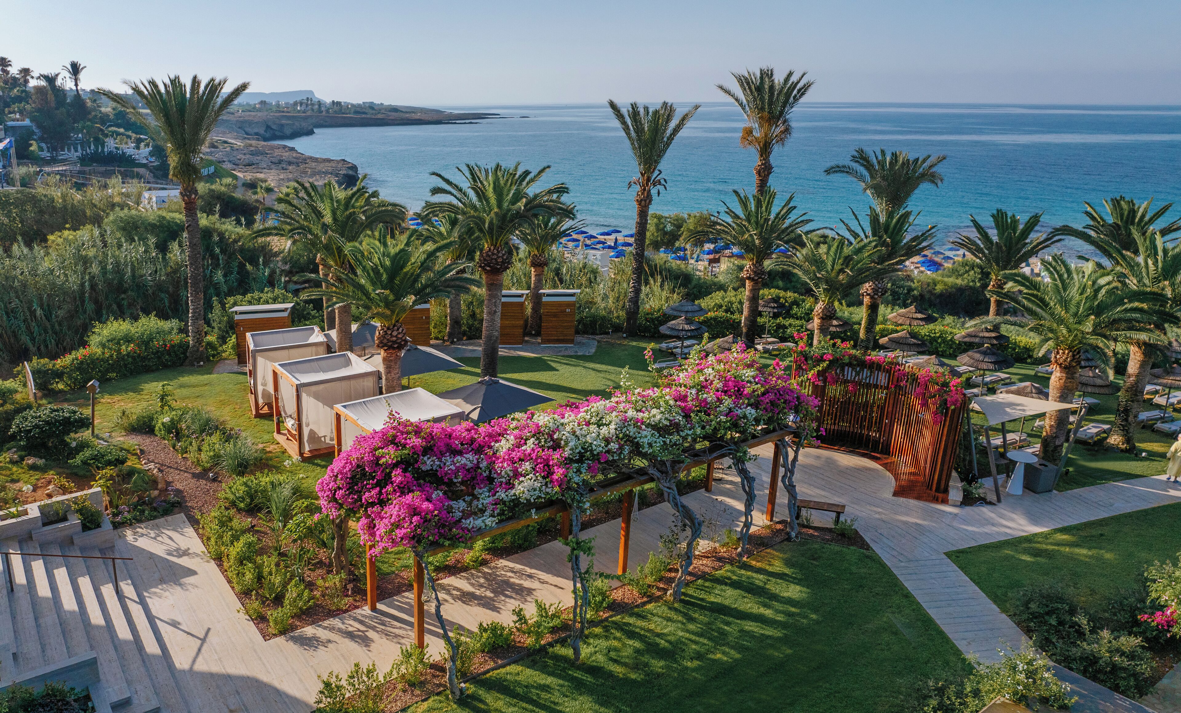 Een resort met uitzicht op de zee, palmbomen en een tuin met bloemen.