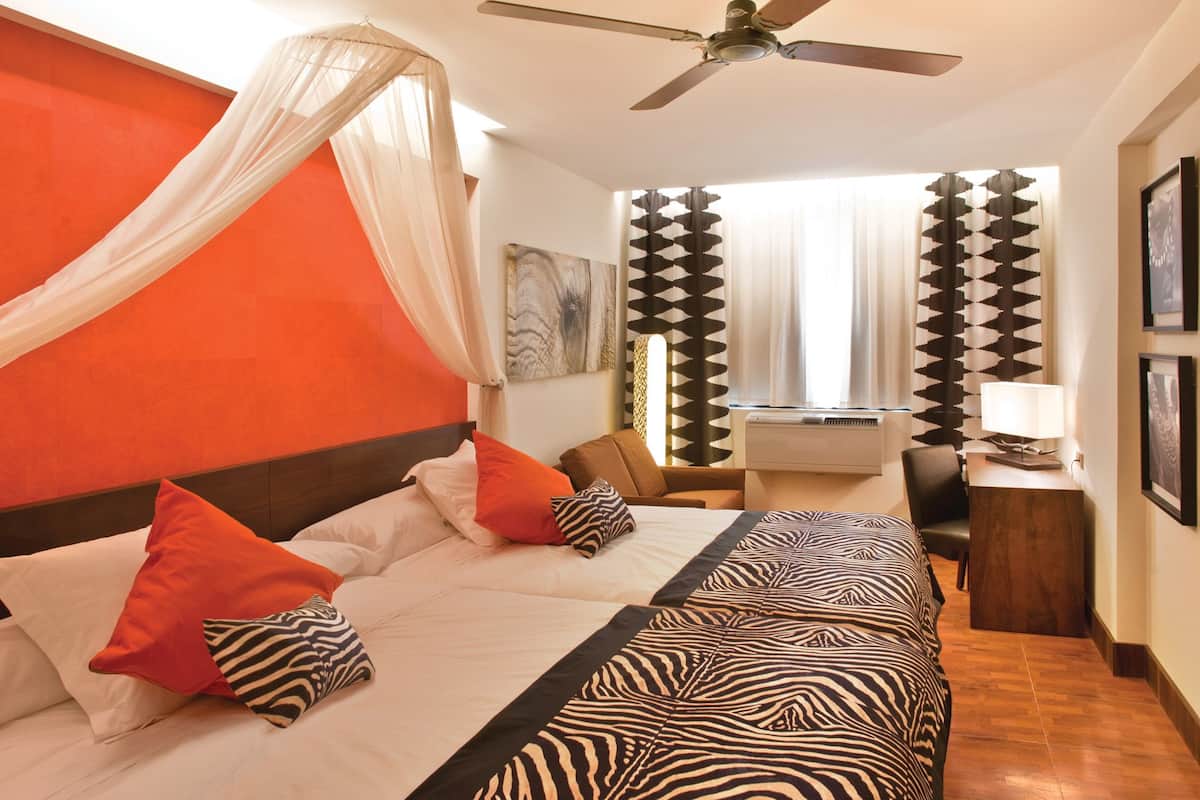 Habitación de hotel con cama, escritorio, silla, ventilador de techo y ventana con cortinas.