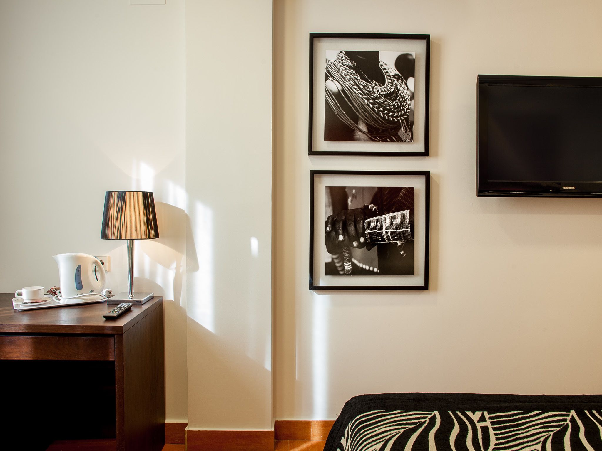 A hotel room with a bed, a desk with a lamp, a coffee maker, and two framed pictures on the wall.