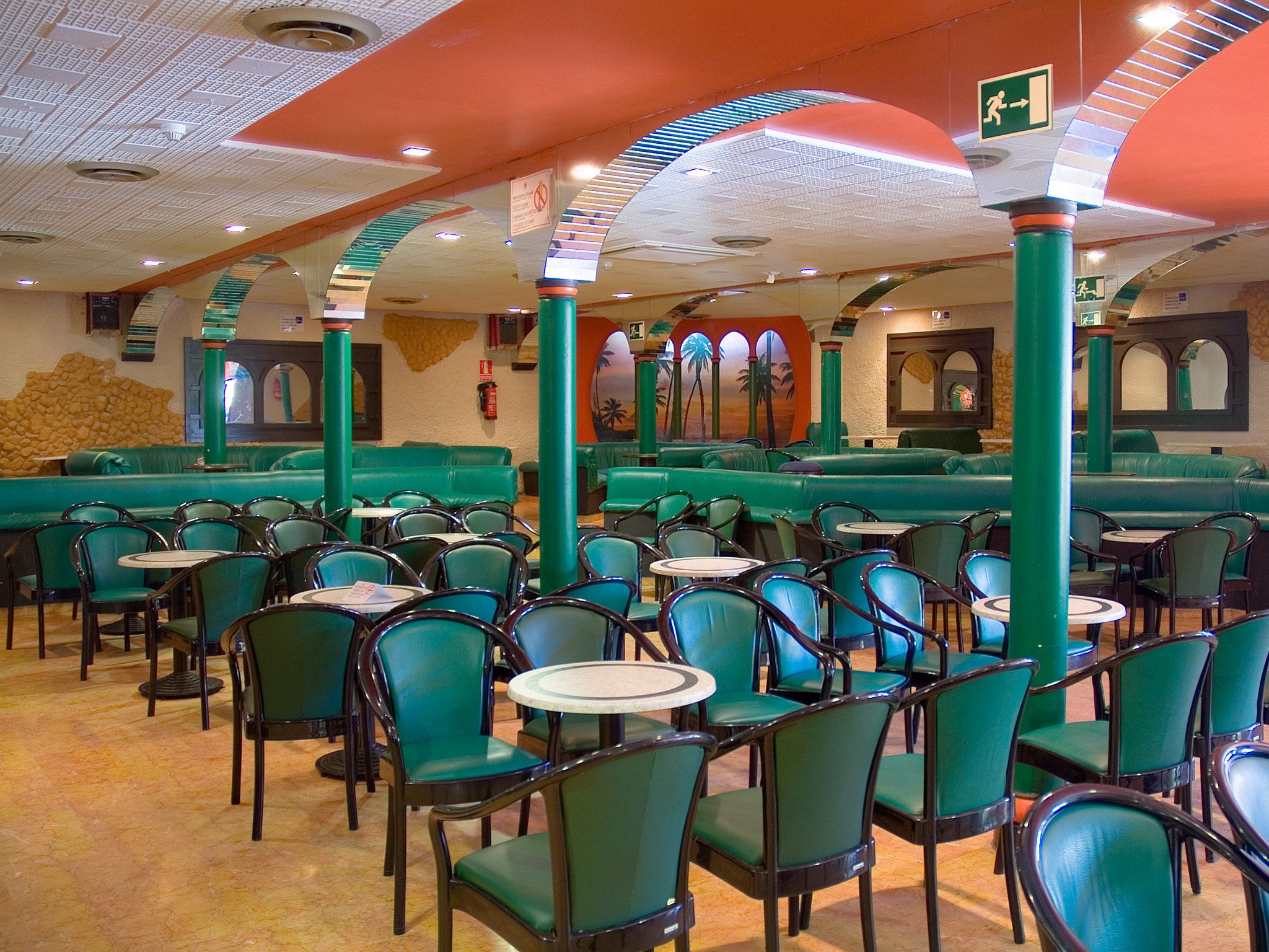 L’intérieur d’un restaurant avec des banquettes et des chaises vertes, un plafond carrelé et un escalier.