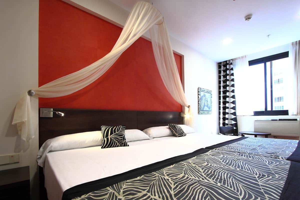 Habitación de hotel con una cama grande, un cabecero rojo y una ventana con cortinas.