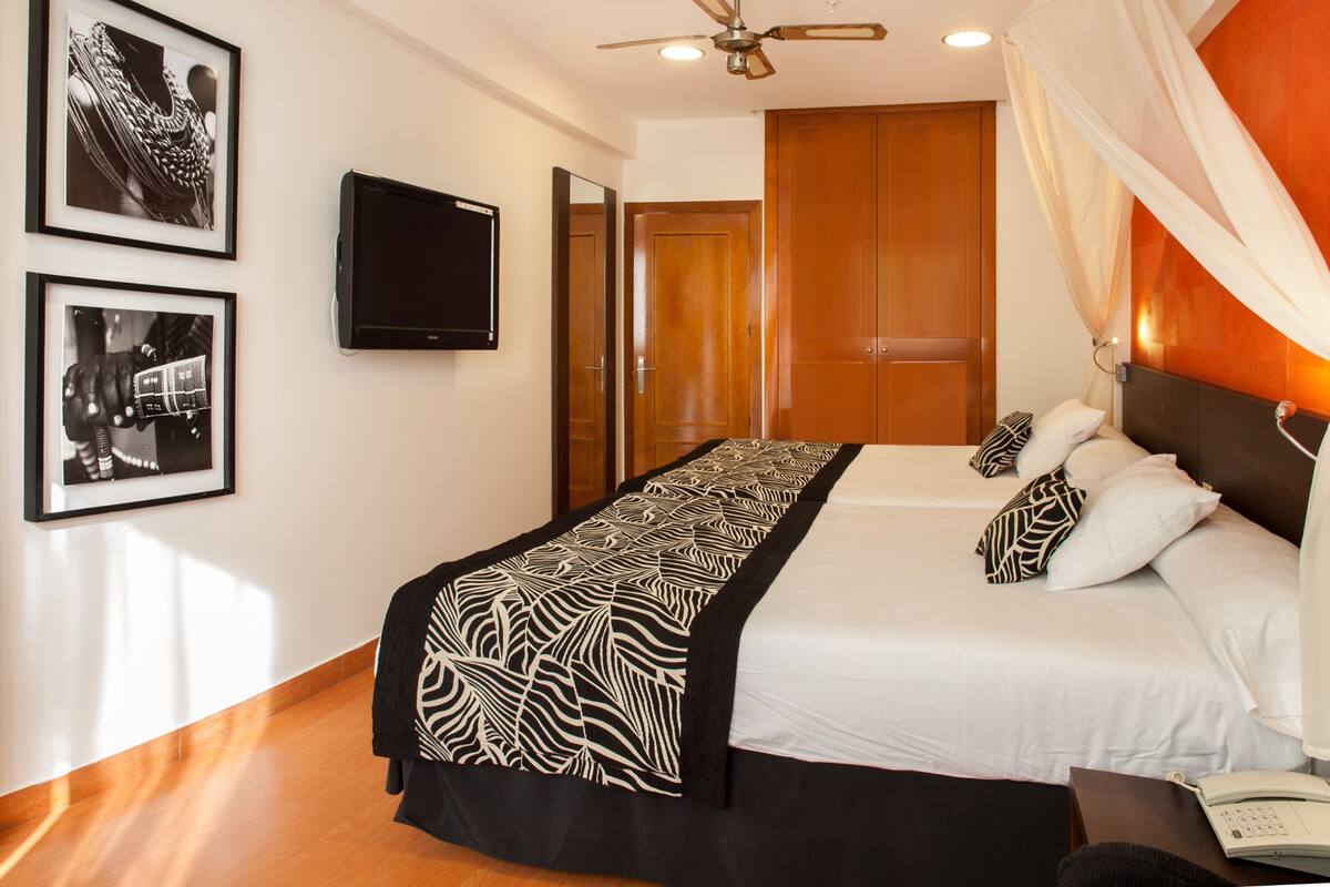 Un dormitorio con cama, televisor, ventilador de techo y armario.