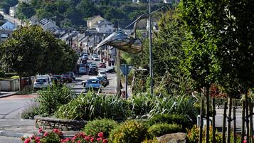 A residential street with parked cars, a metal sculpture, and lush greenery.