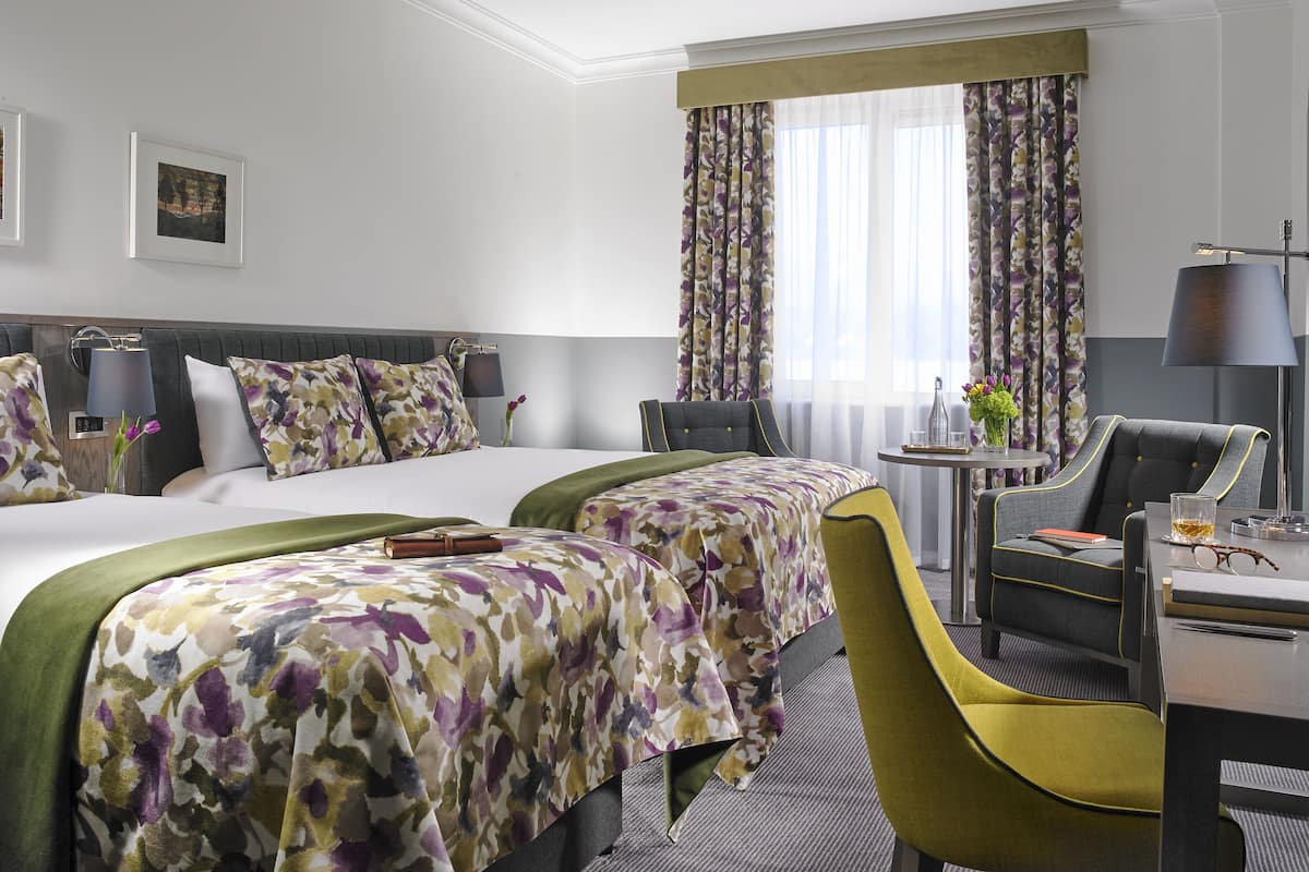 Ein Hotelzimmer mit zwei Betten, einem Schreibtisch, einem Stuhl und einer Lampe.