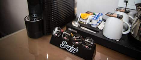 A coffee machine, a coffee cup, a box of coffee pods, and a tray with coffee cups and a kettle on a table.