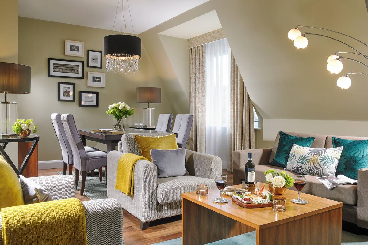 Ein modernes Wohnzimmer mit Essbereich, ausgestattet mit einer Kronleuchter, Sofas und einem Couchtisch mit Blumenarrangement.