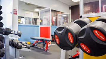 Een sportschool met gewichthefapparatuur, waaronder dumbbells en een bank.