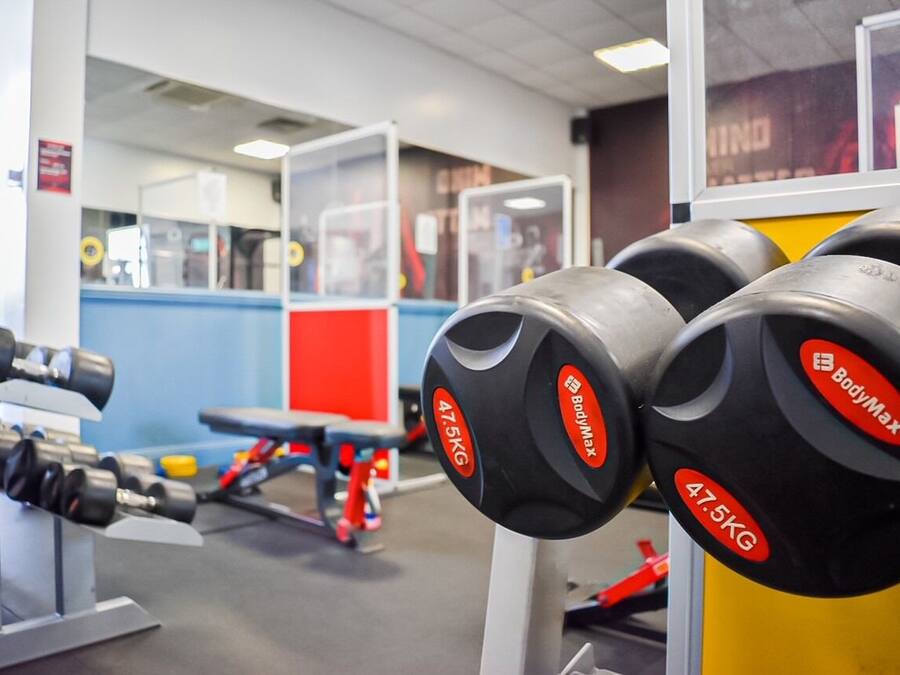 Een sportschool met gewichthefapparatuur, waaronder dumbbells en een bank.