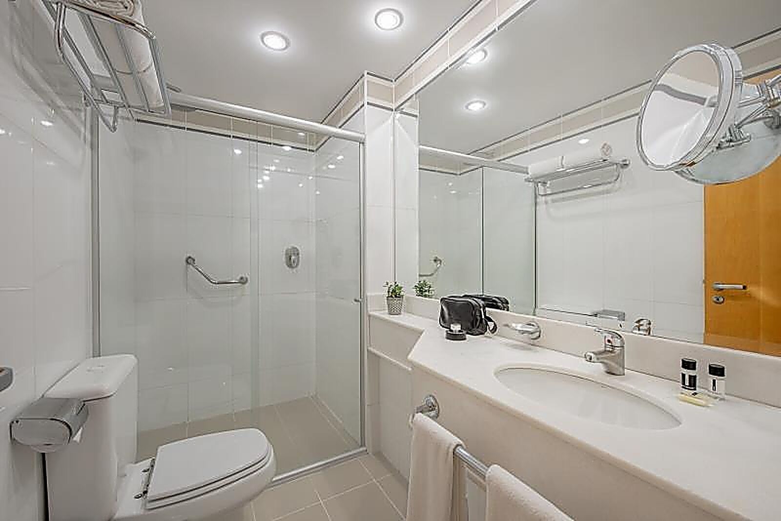 Um banheiro moderno com box de vidro, vaso sanitário, pia com espelho e porta-toalhas.