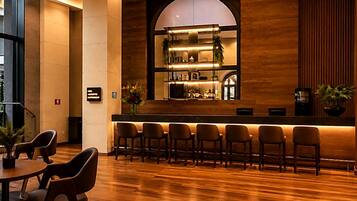 Een bar met een lange toonbank, meerdere stoelen en een houten wand met een groot rondboogvenster.