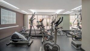 Ett gym med olika konditionsmaskiner, utrustning för styrketräning och en stor informationsaffisch på väggen.