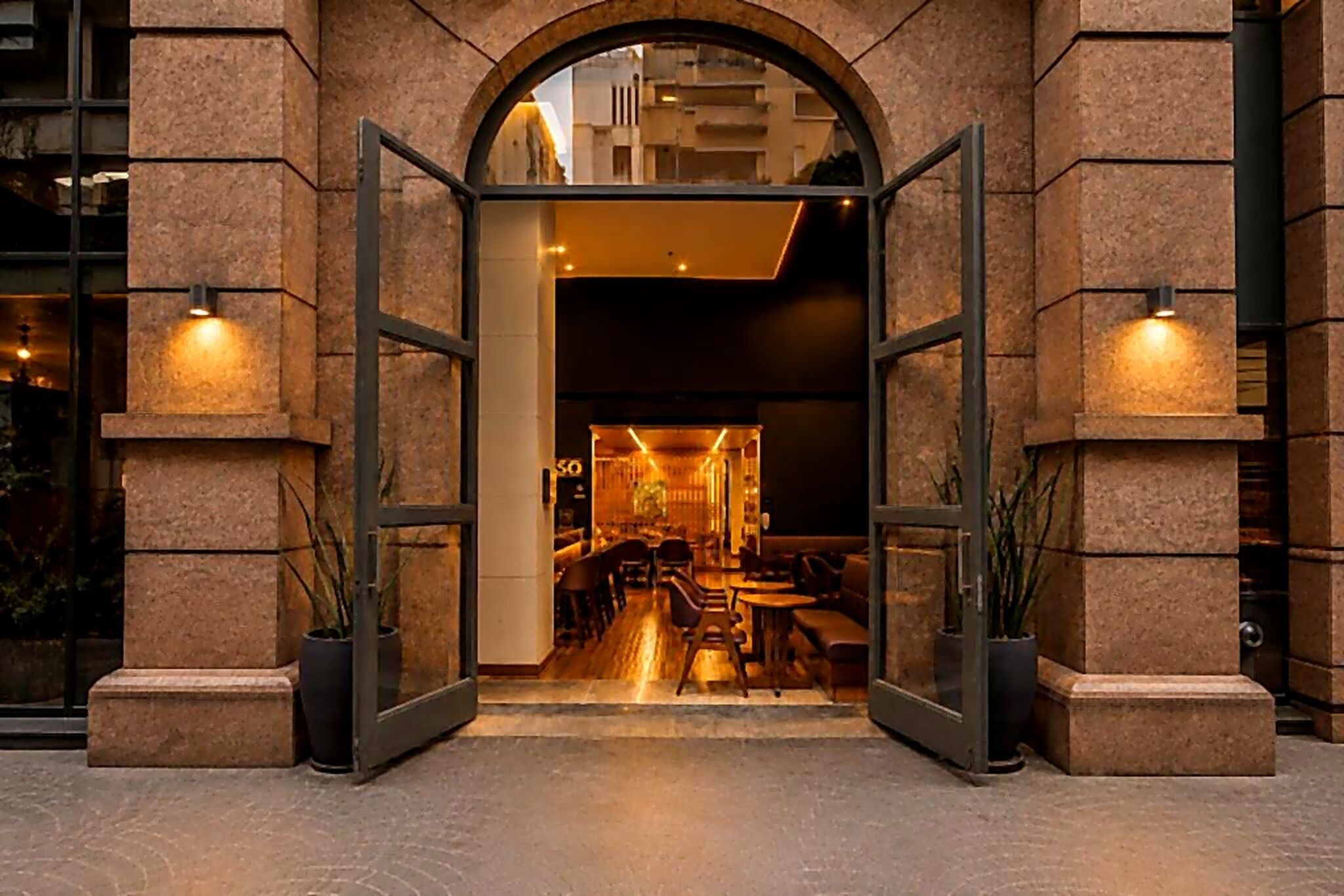 An open entrance to a restaurant with a modern interior, stone walls, and potted plants.