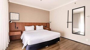 Ett hotellrum med en stor säng, sängbord, en spegel och ett trägolv.