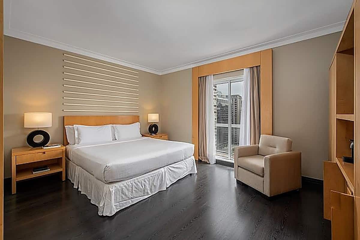 Een hotelkamer met een groot bed, nachtkastjes met lampen, een stoel en een raam met gordijnen.