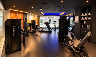 A gym with various exercise equipment, including treadmills and weight machines, and a wall with a towel rack.