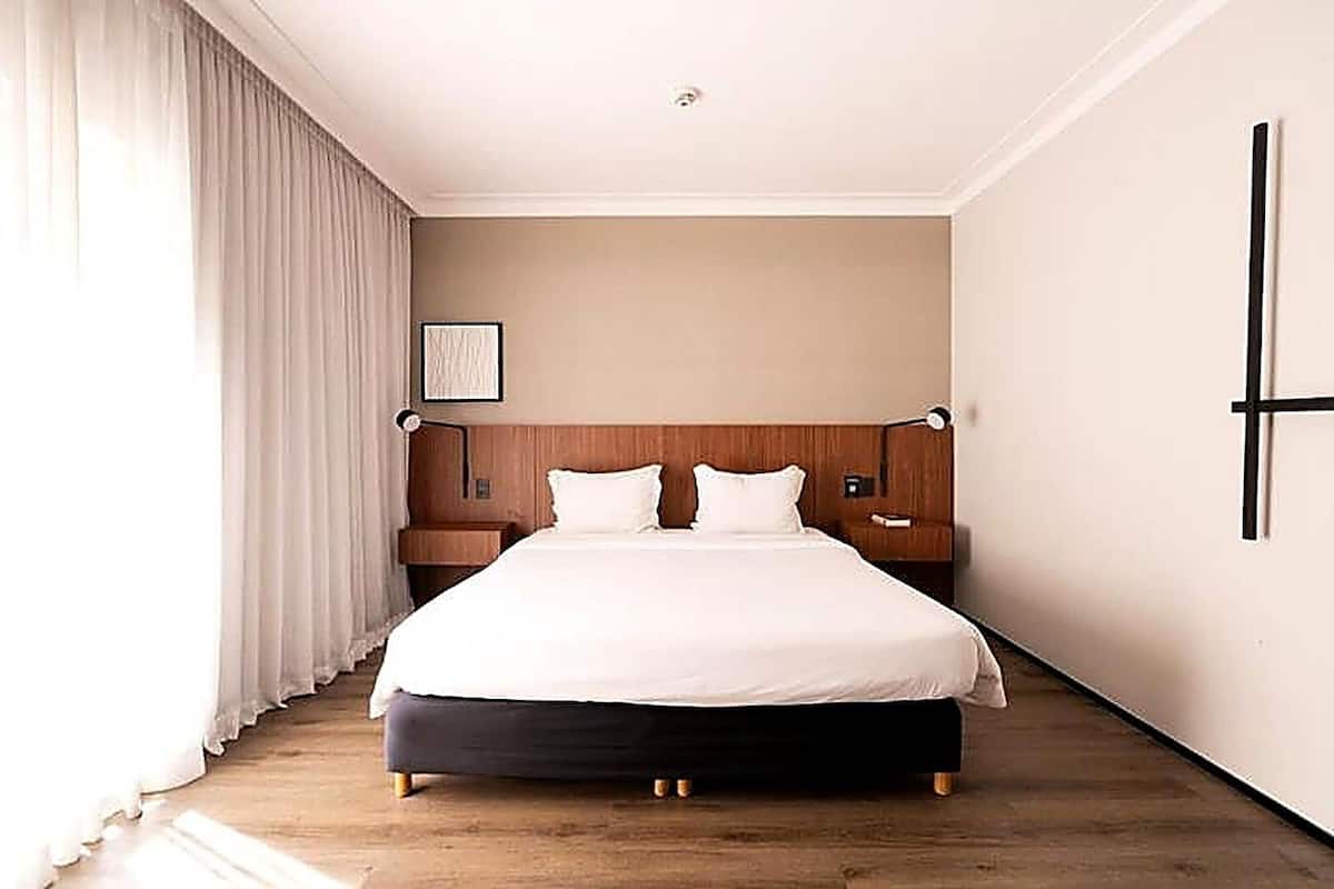 Een hotelkamer met een groot bed, een houten hoofdeinde, nachtkastjes en uitzicht op het omliggende landschap.