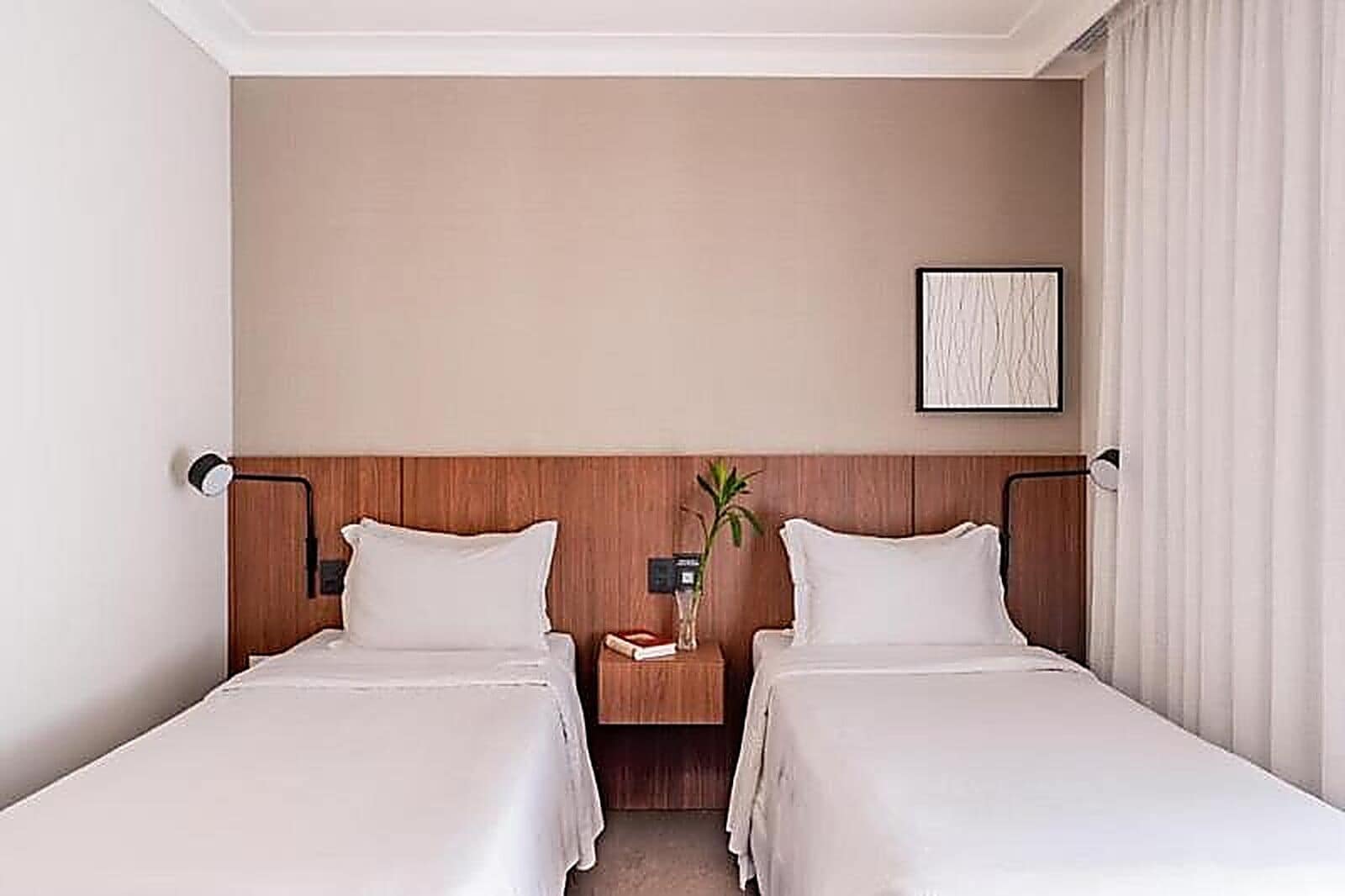 A hotel room with two beds, wooden headboards, a nightstand with a lamp, and a framed picture on the wall.