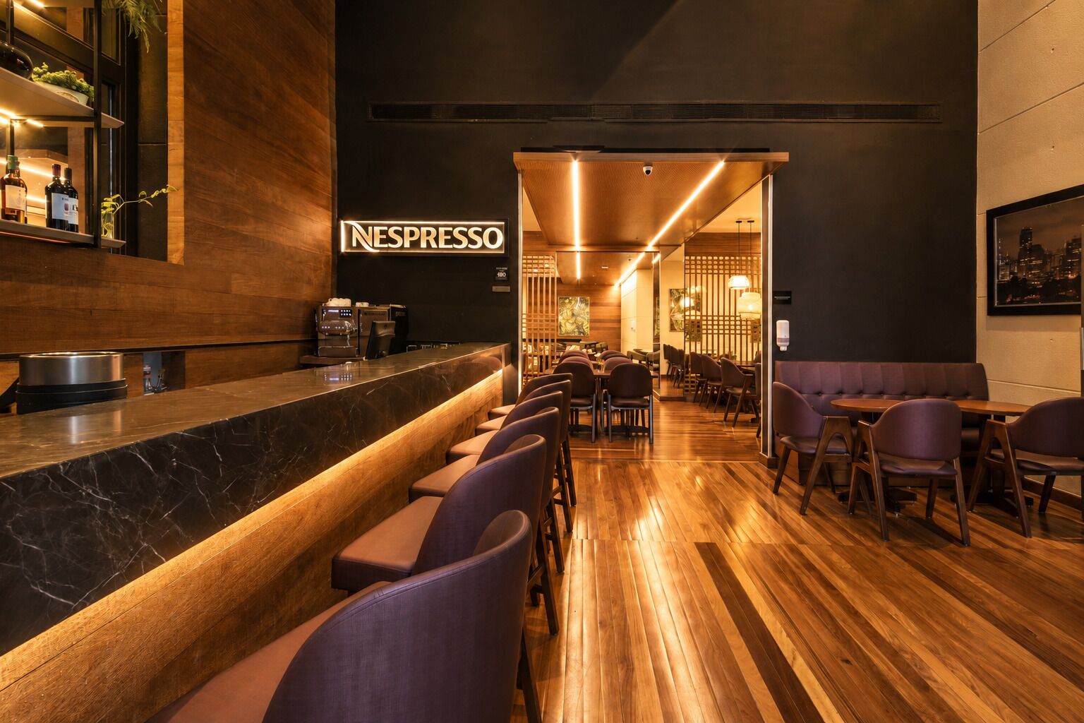 Un espace bar moderne doté d’une machine Nespresso, de sièges et d’un plancher en bois.