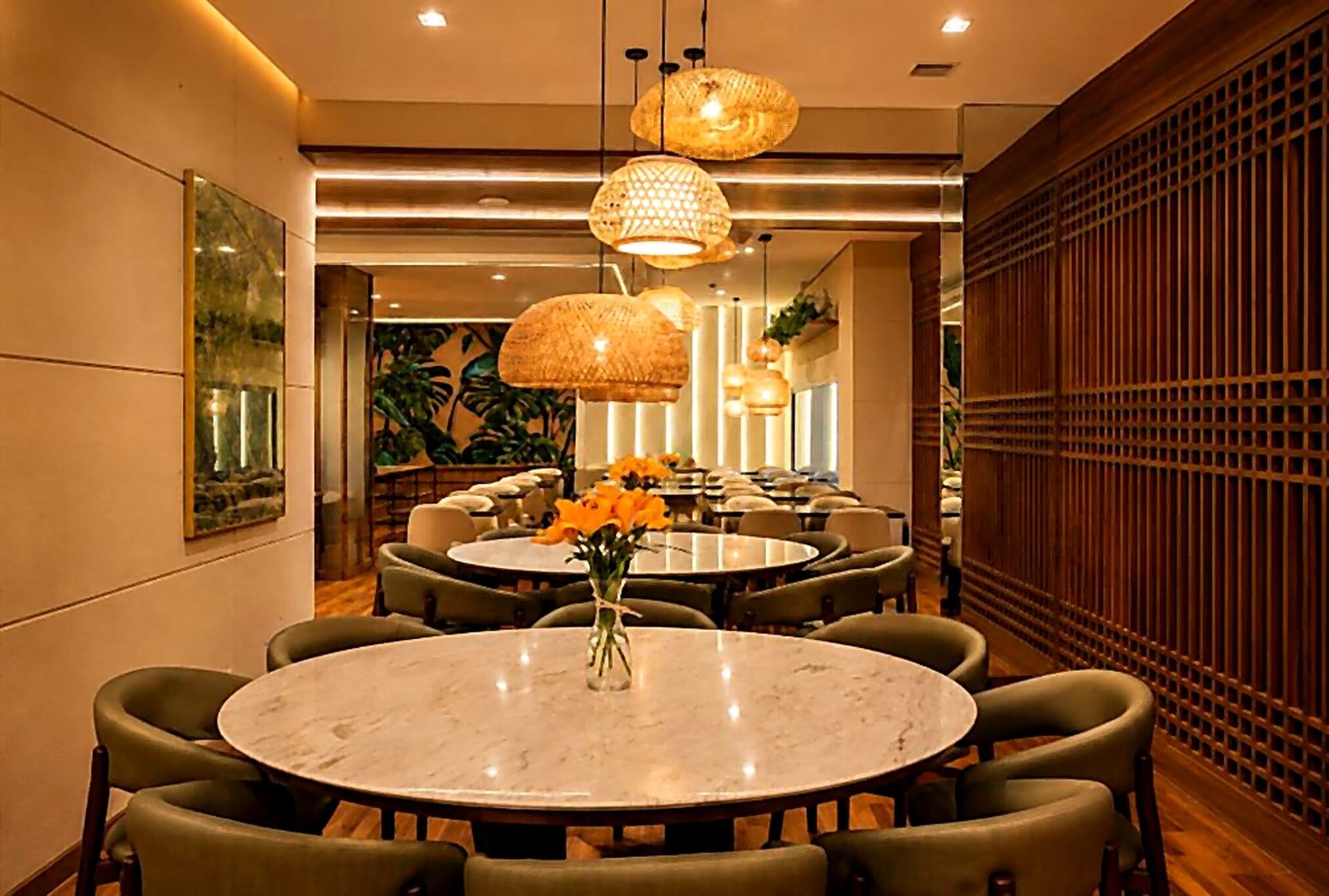 A dining area with round tables, green upholstered chairs, and hanging rattan lamps.