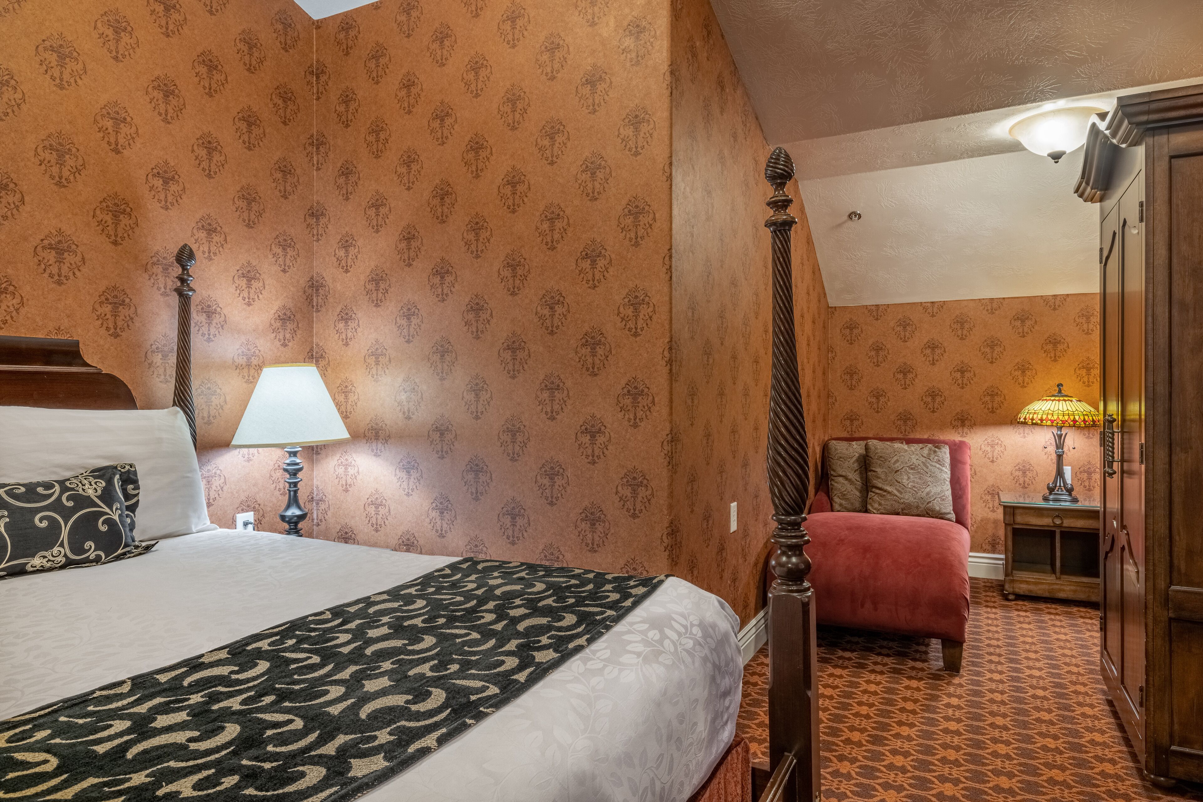 A hotel room with a bed, bedside table, lamp, and a wardrobe.
