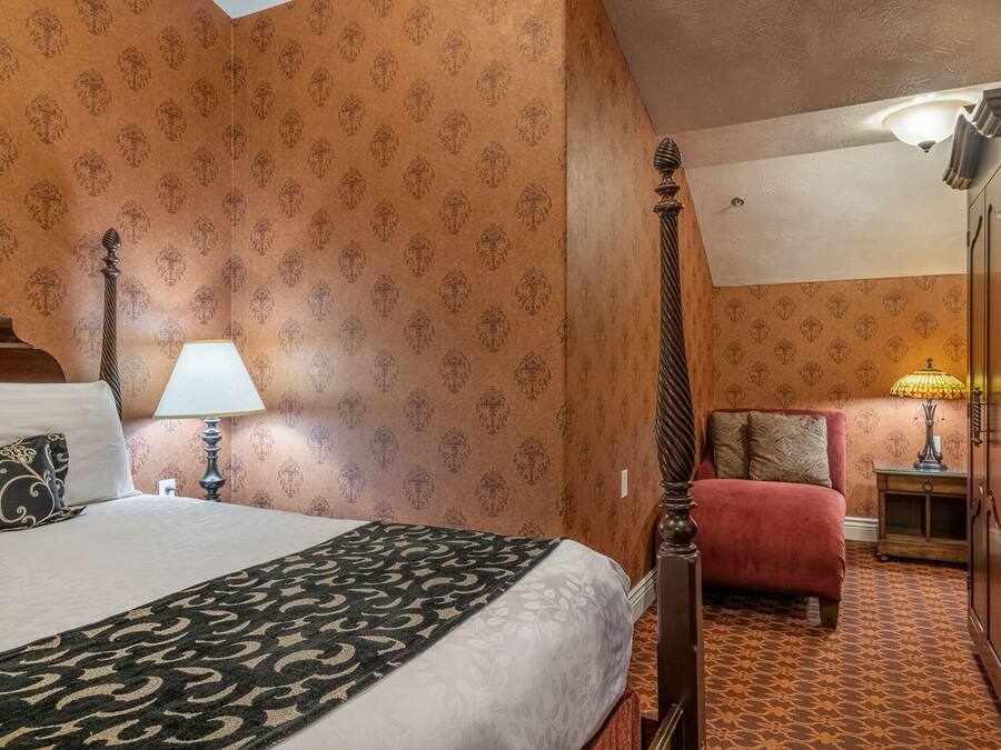 A hotel room with a bed, bedside table, lamp, and a wardrobe.