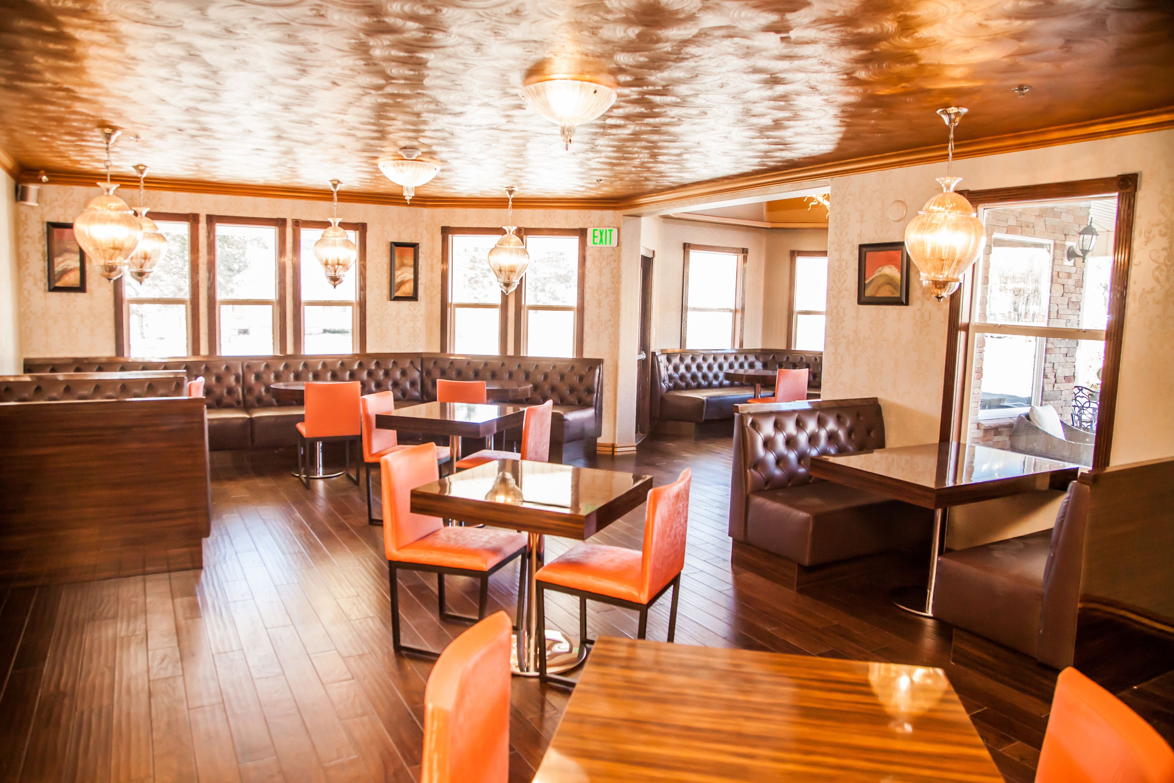 A restaurant with wooden flooring, booths, and tables with orange chairs.