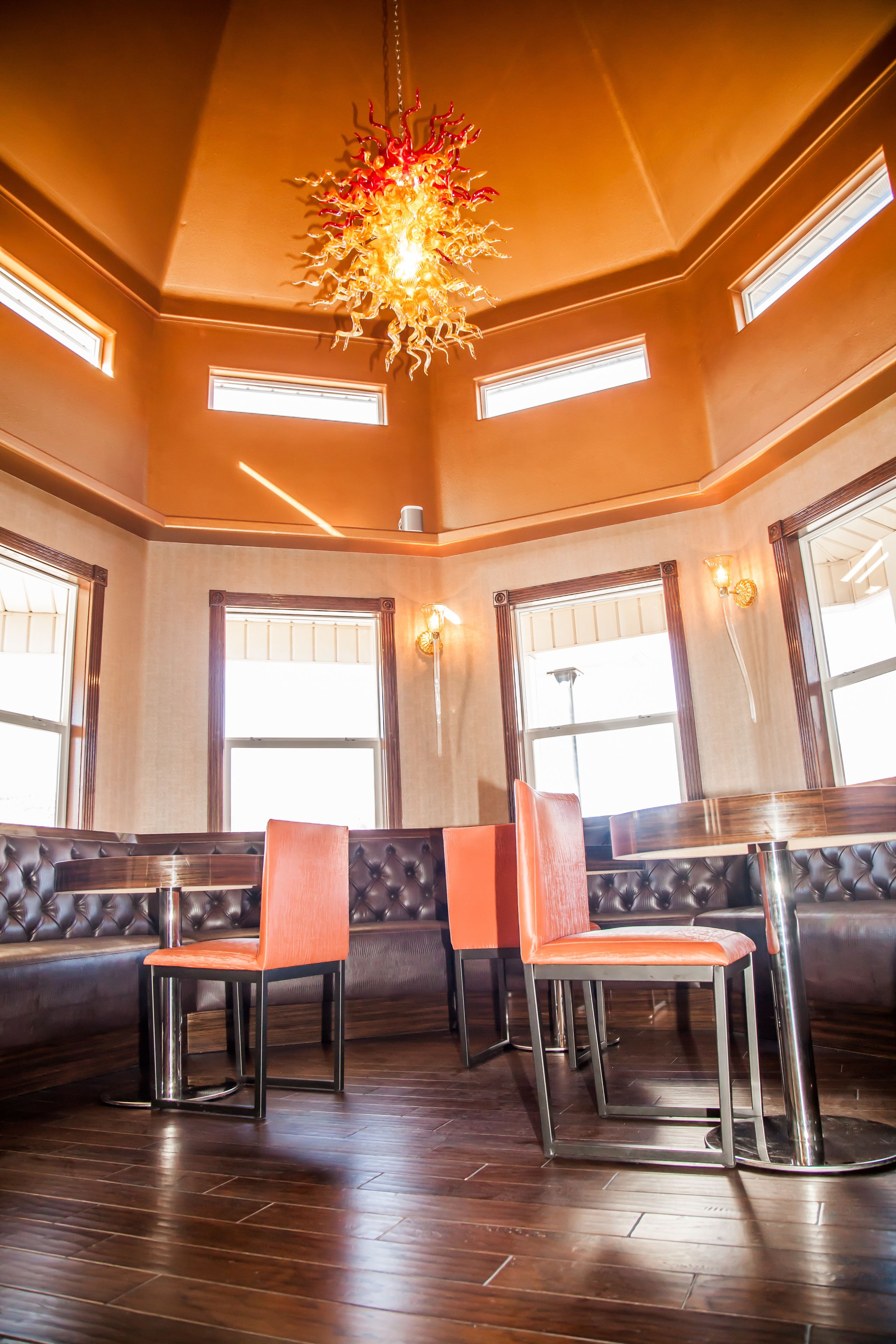 A restaurant interior with a high ceiling, a chandelier, and a seating area with cushioned booths and chairs.