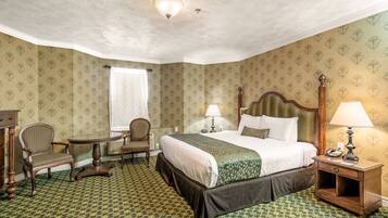 A hotel room with a large bed, two chairs, a small table, and a nightstand with a lamp.