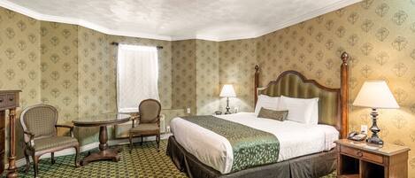 A hotel room with a large bed, two chairs, a small table, and a nightstand with a lamp.