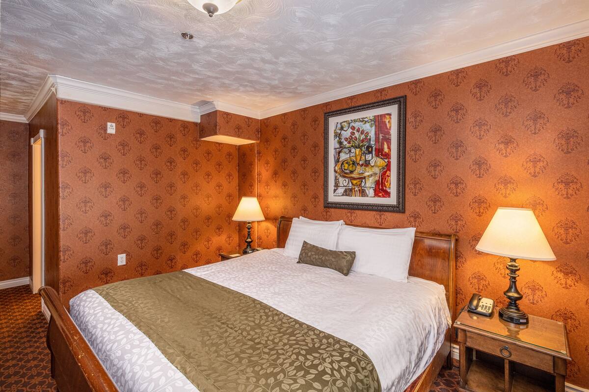 Habitación de hotel con una cama grande, dos lámparas de noche, una mesita de noche con un teléfono y un cuadro en la pared.