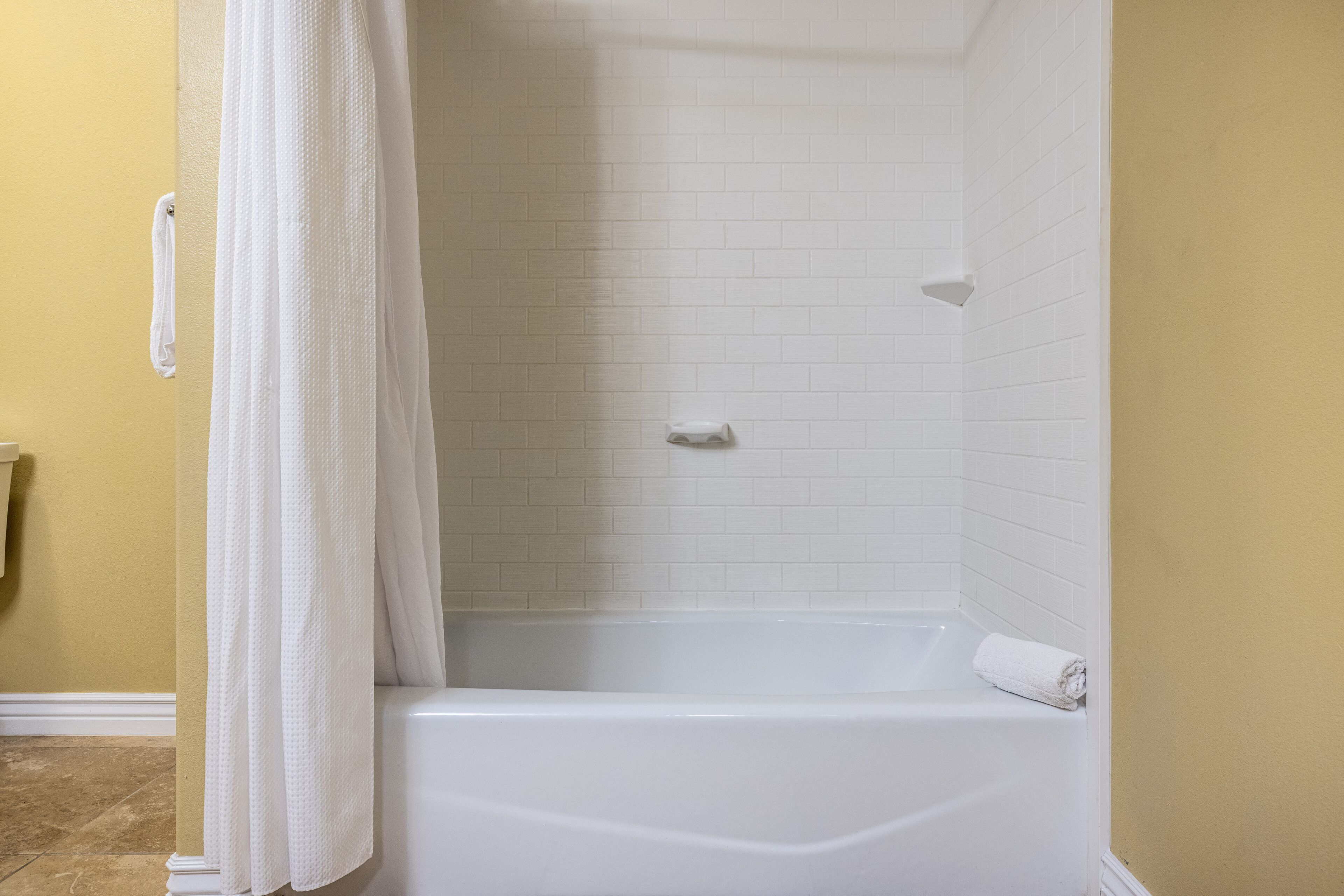 A bathroom with a white bathtub, a shower curtain, and a towel on the tub.