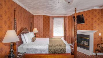 A four-poster bed with a wooden headboard, a bedside table with a lamp, a fireplace, and a television mounted on the wall.