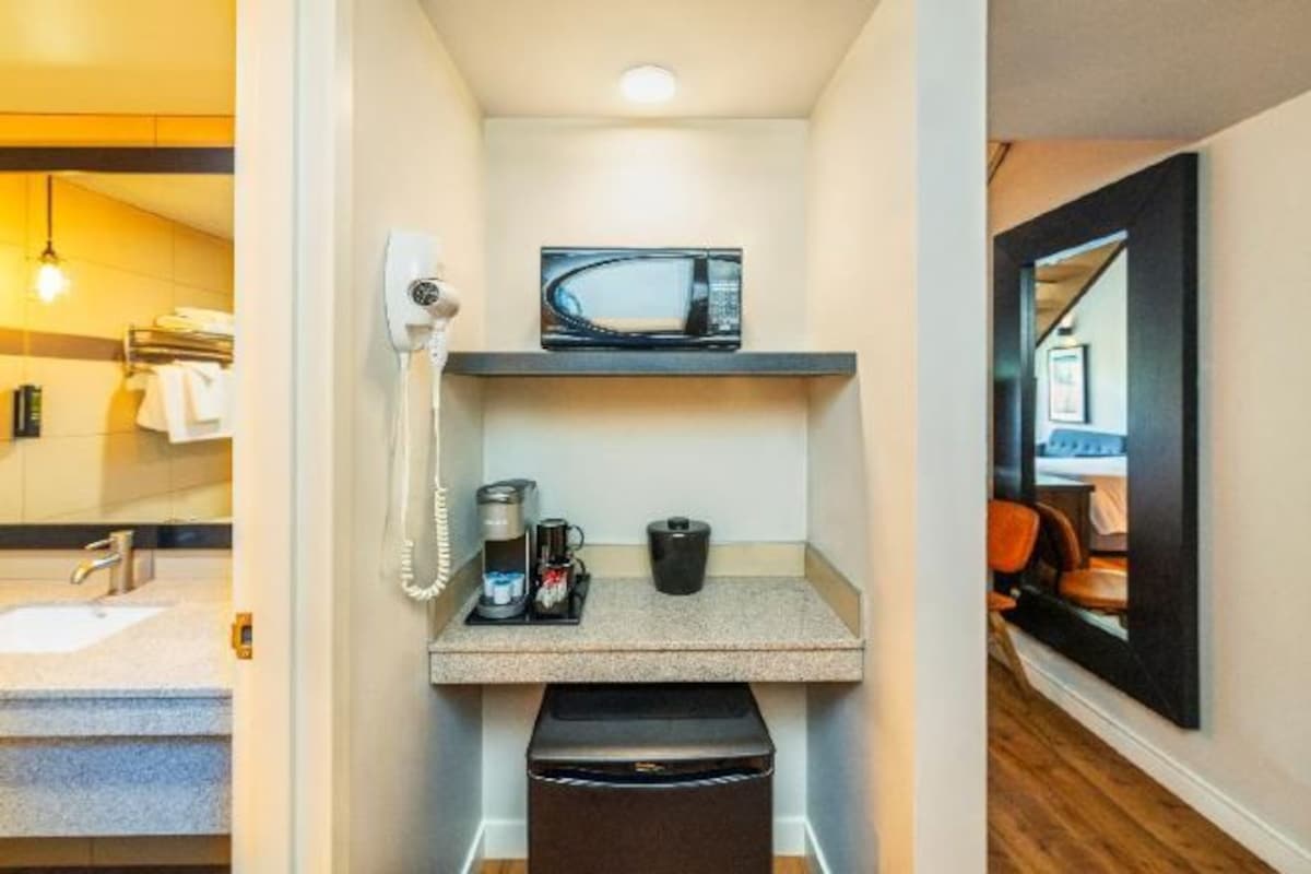 Habitación de hotel compacta con microondas, cafetera y teléfono en un estante.