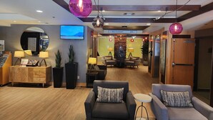 Un hall de hotel con mostrador de recepción, zona de estar y un televisor que muestra una vista panorámica.