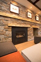 A stone fireplace with framed pictures above it, a dark-colored sofa, and a wooden floor.