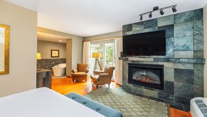 Una habitación de hotel moderna con chimenea, televisión, cama y dos sillones.