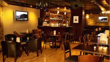 Zona de bar con suelo de madera, asientos de cuero y mostrador con botellas.