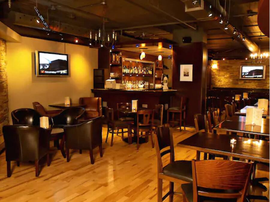 Zona de bar con suelo de madera, asientos de cuero y mostrador con botellas.