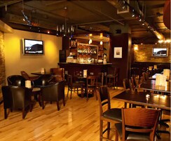 A bar area with wooden flooring, leather seating, and a bar counter with bottles.
