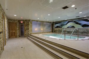 Una piscina interior con pared de piedra, puerta de madera y mampara de vidrio.