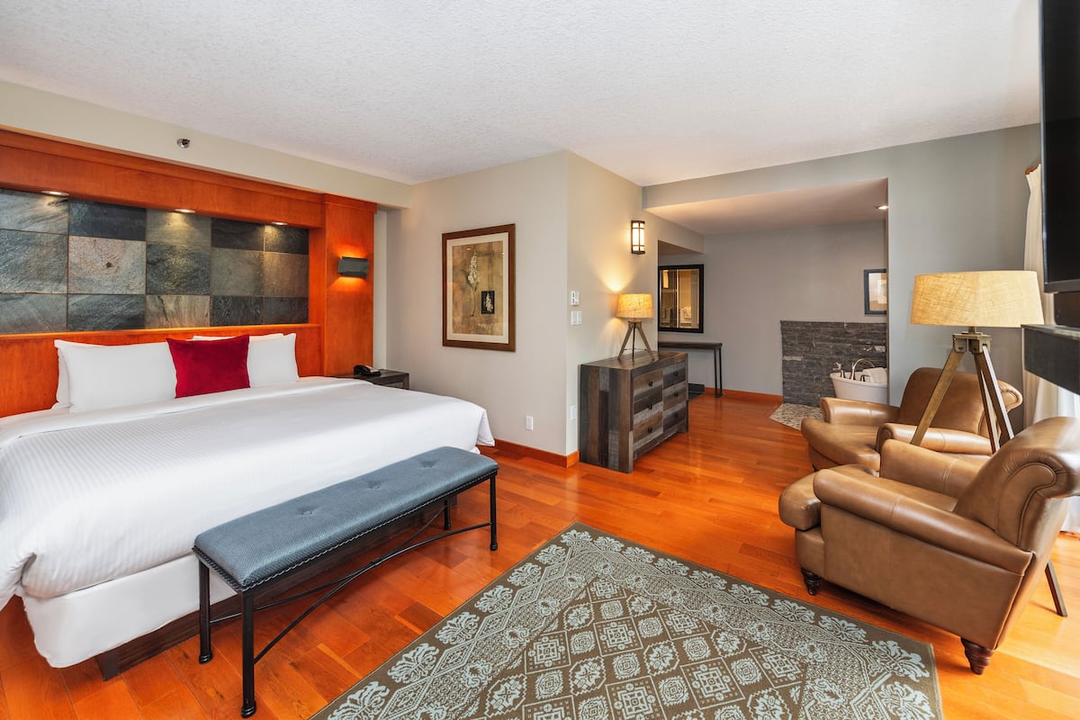A hotel room with a large bed, a bench, a sofa, and a fireplace.