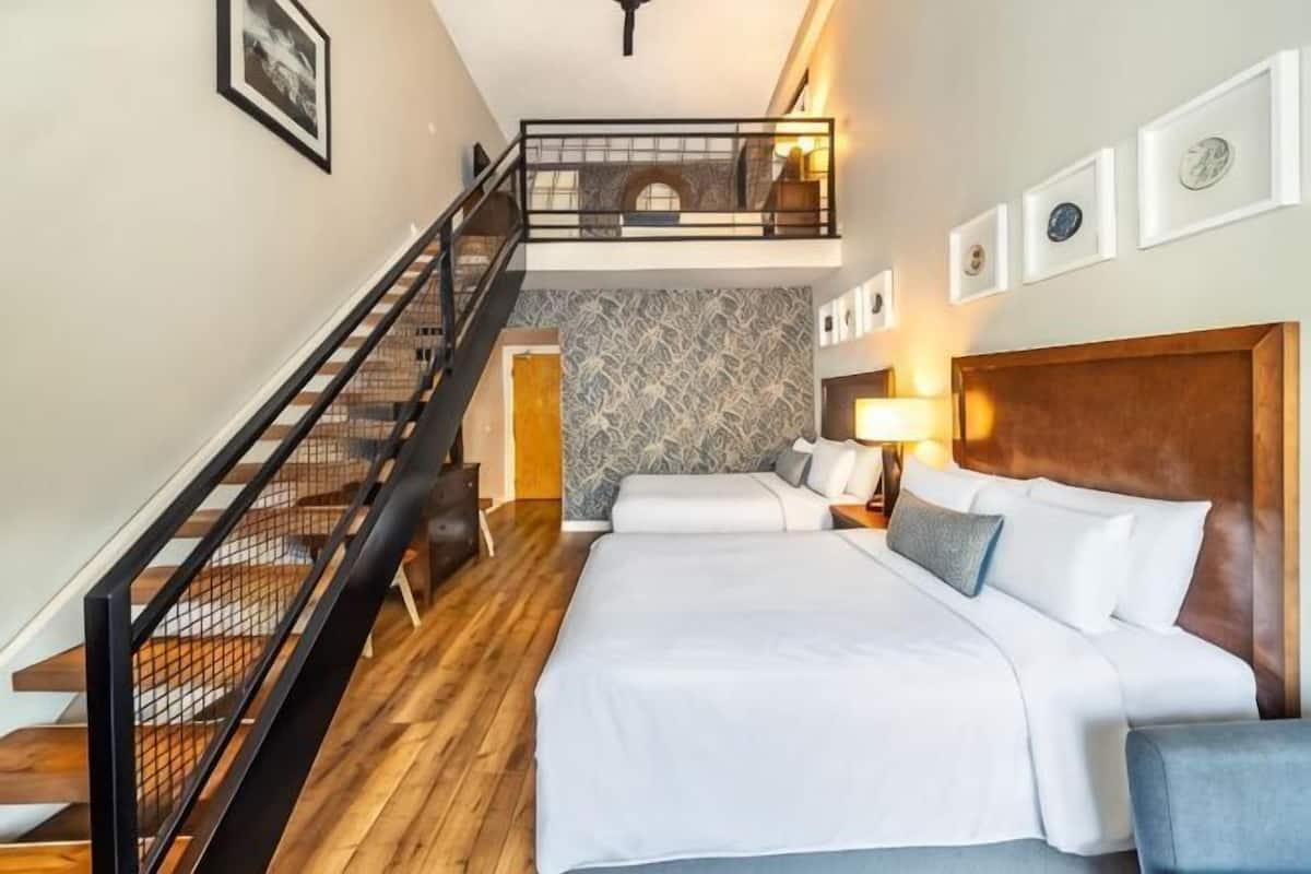 A hotel room with a bed, a nightstand, a lamp, a staircase, and a view of the city.