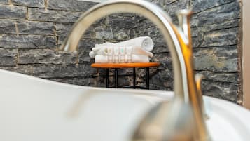 A bathroom with a stone wall, a white bathtub, and a towel rack with towels.