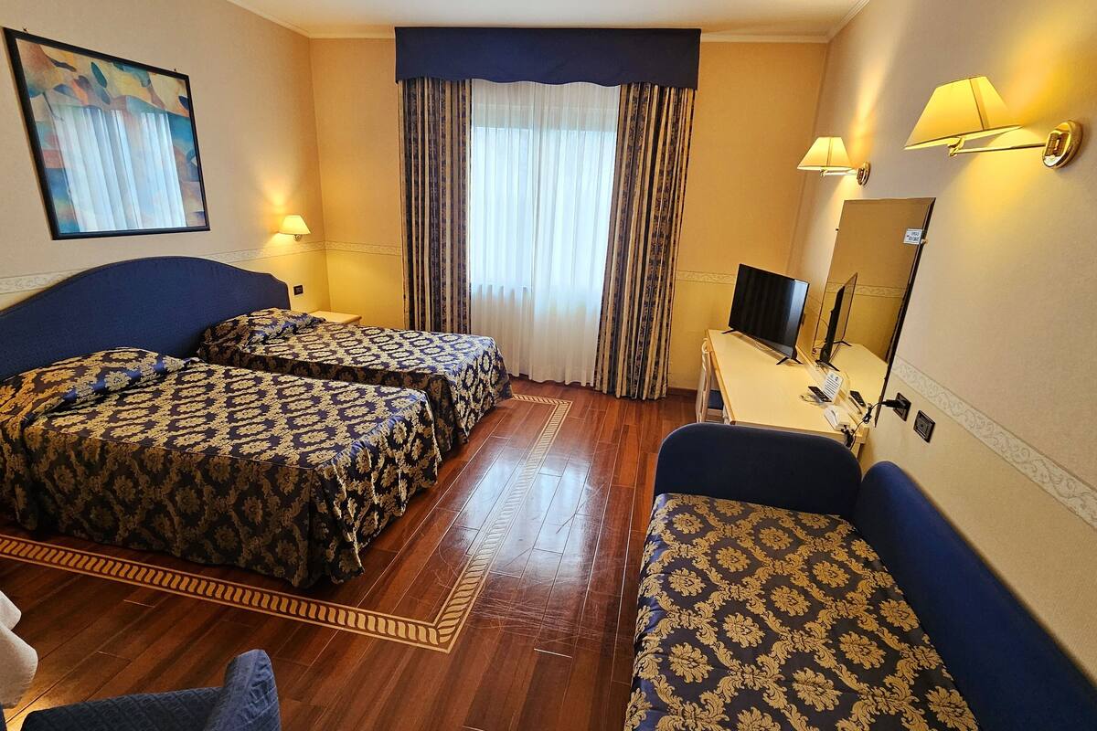 A hotel room with two beds, a desk with a computer, a TV, and a mirror.