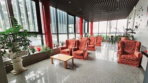 A spacious lobby with a polished granite floor, red patterned chairs, a wooden table, and large windows offering views of the street. - Ai Tigli (Langhirano)