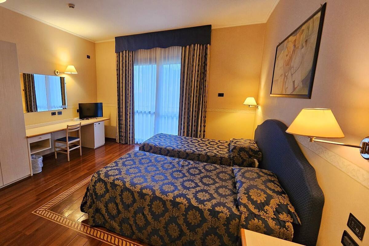 A hotel room with a desk, two beds, a television, and a window with curtains.