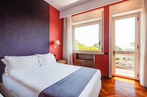 Een hotelkamer met een bed, nachtkastje, raam met uitzicht op de omgeving, en een balkon.